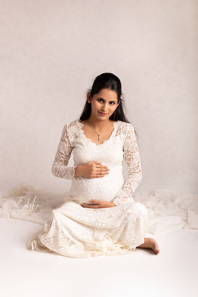 Gorgeous mom to be in white outfit sitting and holding belly photography in Pune