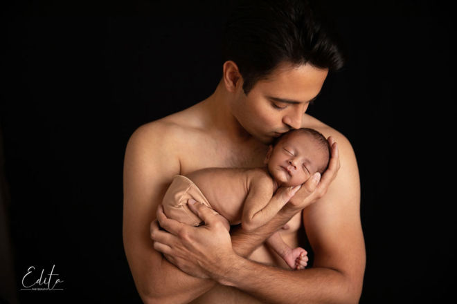 Shirtless dad holding and kissing newborn baby