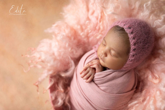 Indian Newborn girl wrapped in pink wrap with pink bonet posed in the bucket