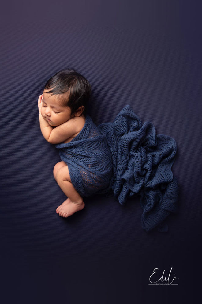 Baby girl in blue knitted wrap, side pose from top aerial shoot