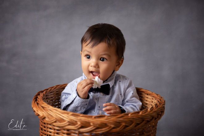 Baby boy in grey shirt with black bow holding flower with grey painted canvas background