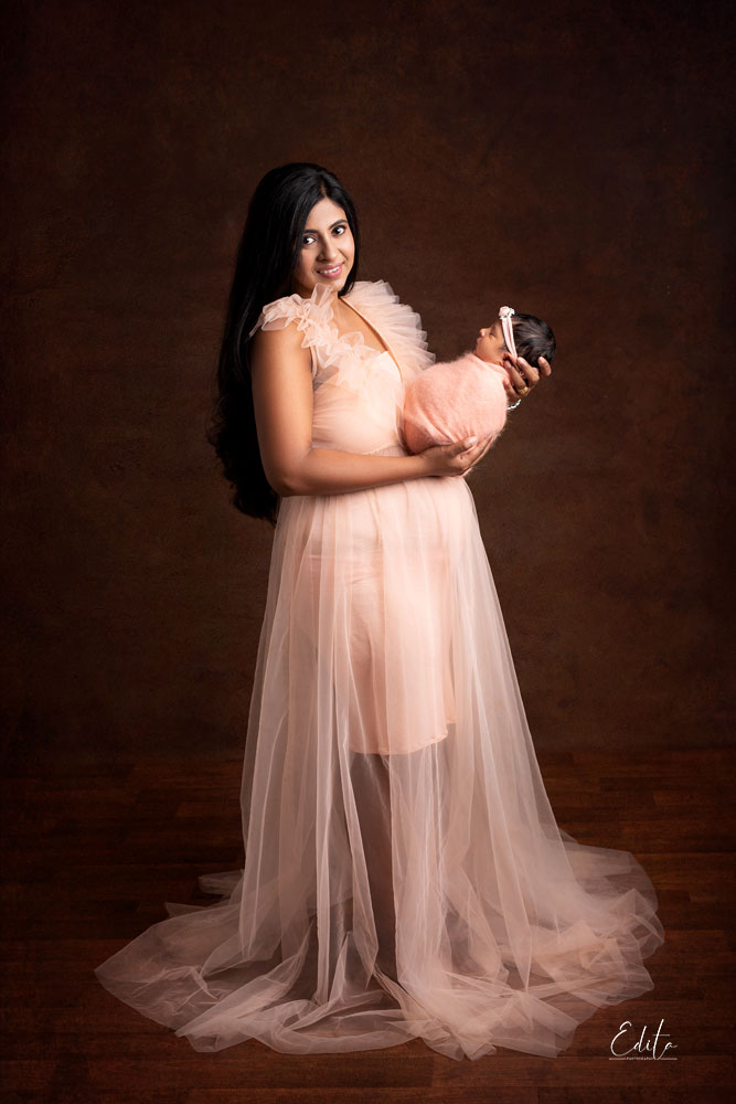 Mother in luxurious peach long gown holding newborn baby girl in Pune. A Happy Mothers Day