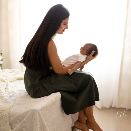 Mom sitting on bed and holding newborn baby girl backlit photo