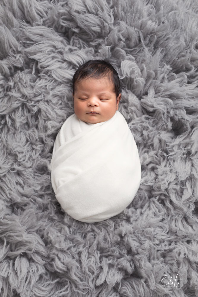 Newborn baby boy in white wrap on grey flokati